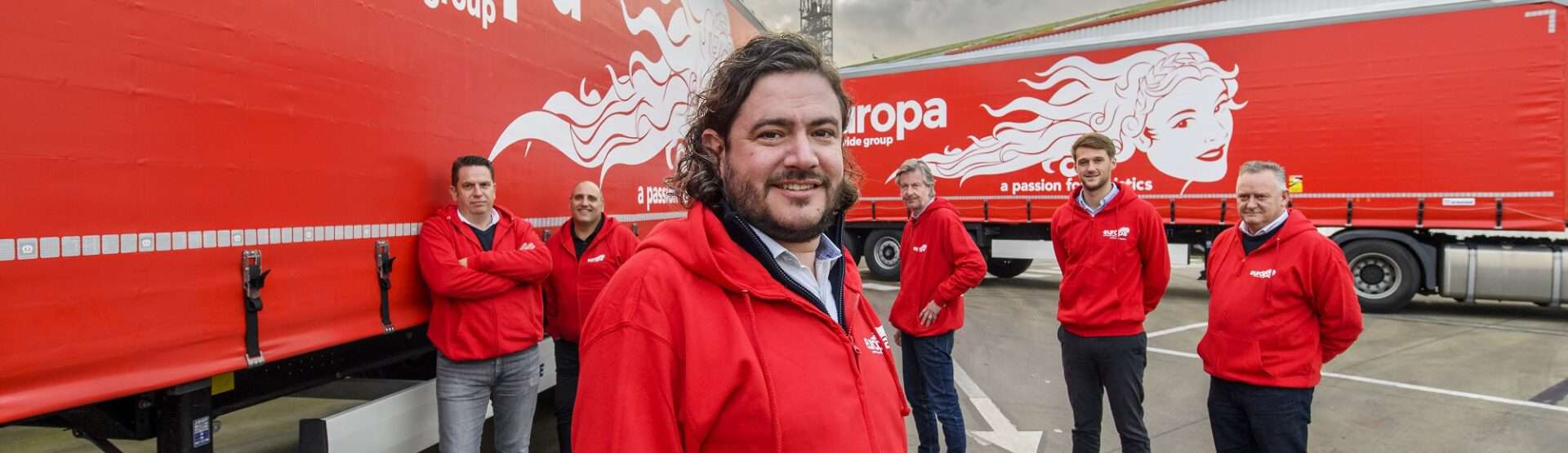 Carlo Turner and team stand in red, branded Europa hoodies in front of two Europa Road trucks.