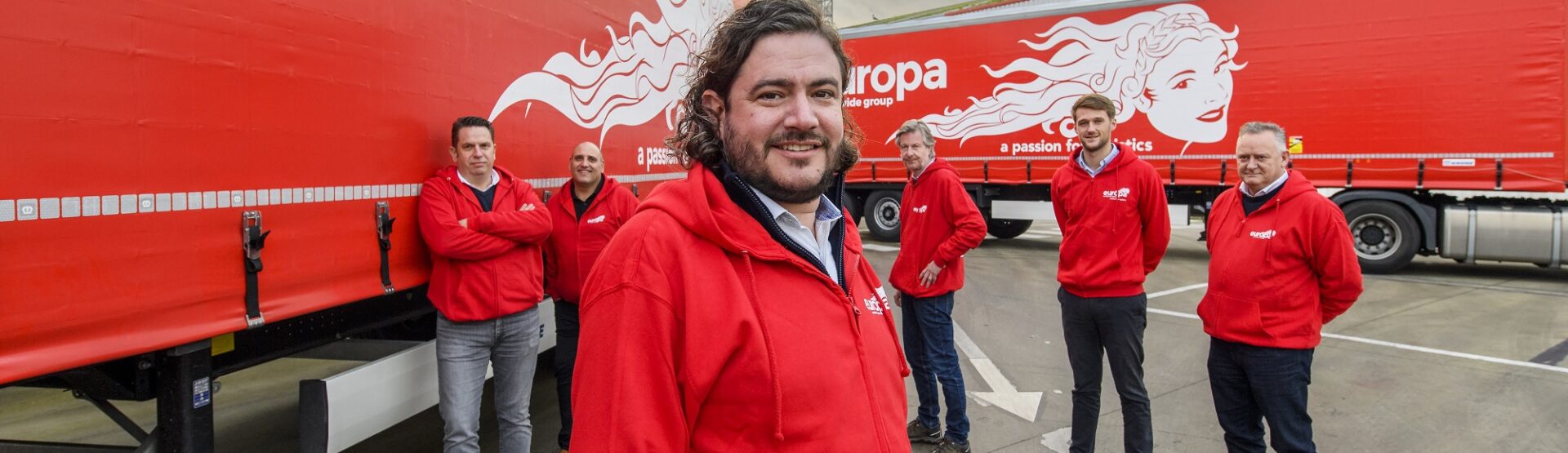 Carlo Turner and team stand in red, branded Europa hoodies in front of two Europa Road trucks.
